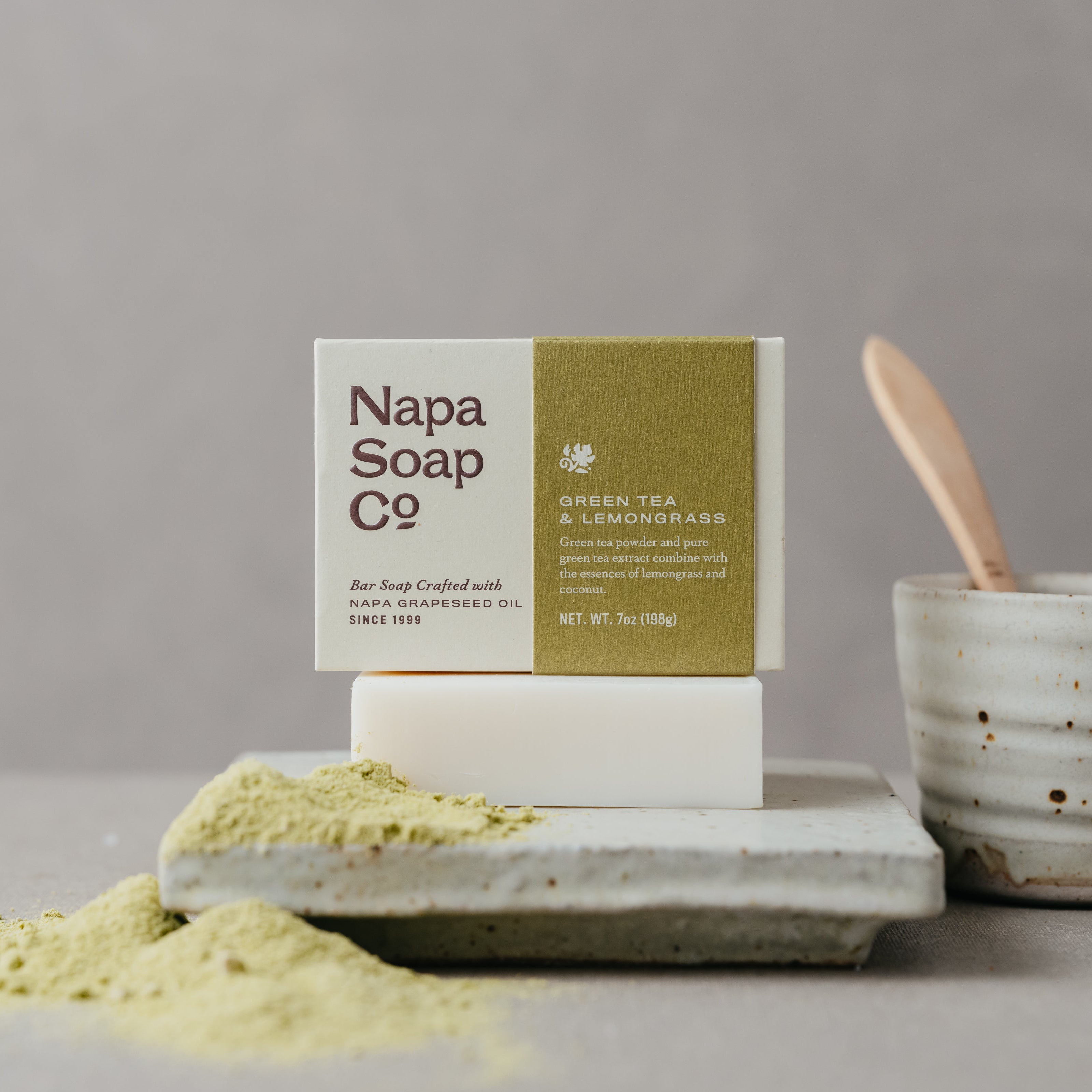 Napa Soap Co bar of soap with a container of green tea and matcha powder on a gray surface.