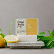 Bar of soap from Napa Soap Co with lemons and lemon verbena leaves on a gray background