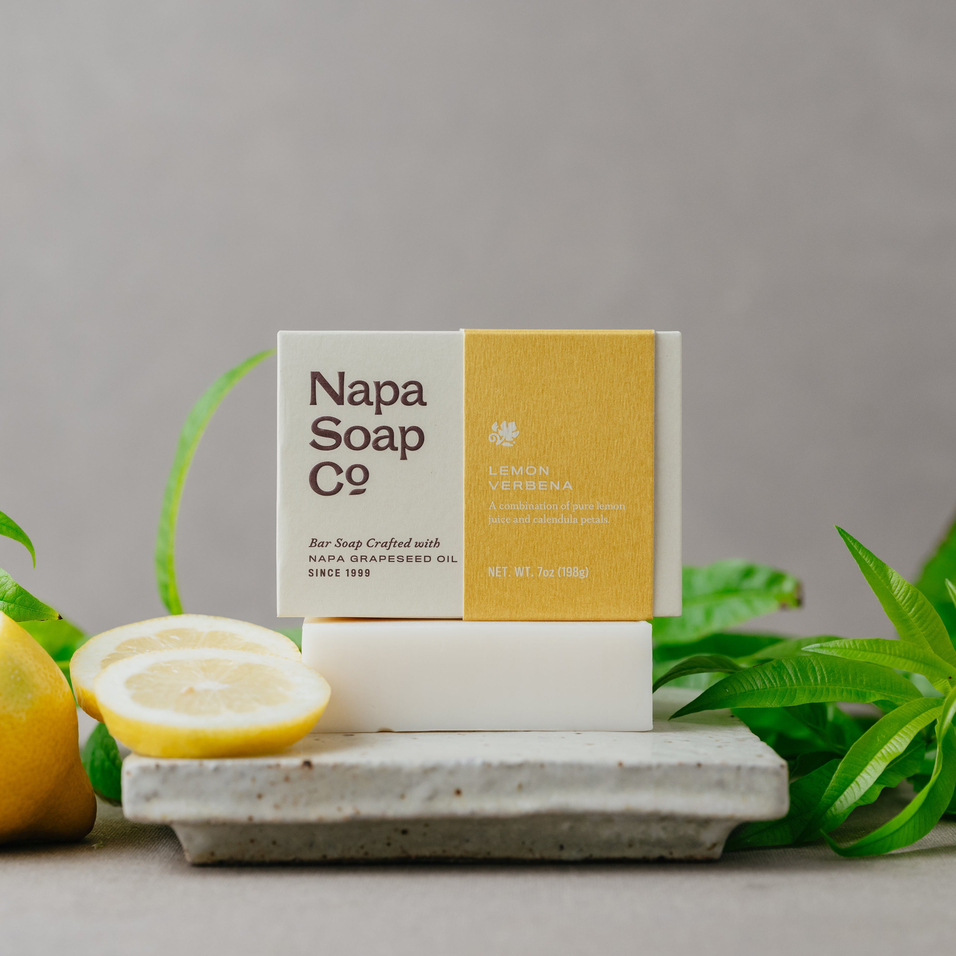 Bar of soap from Napa Soap Co with lemons and lemon verbena leaves on a gray background
