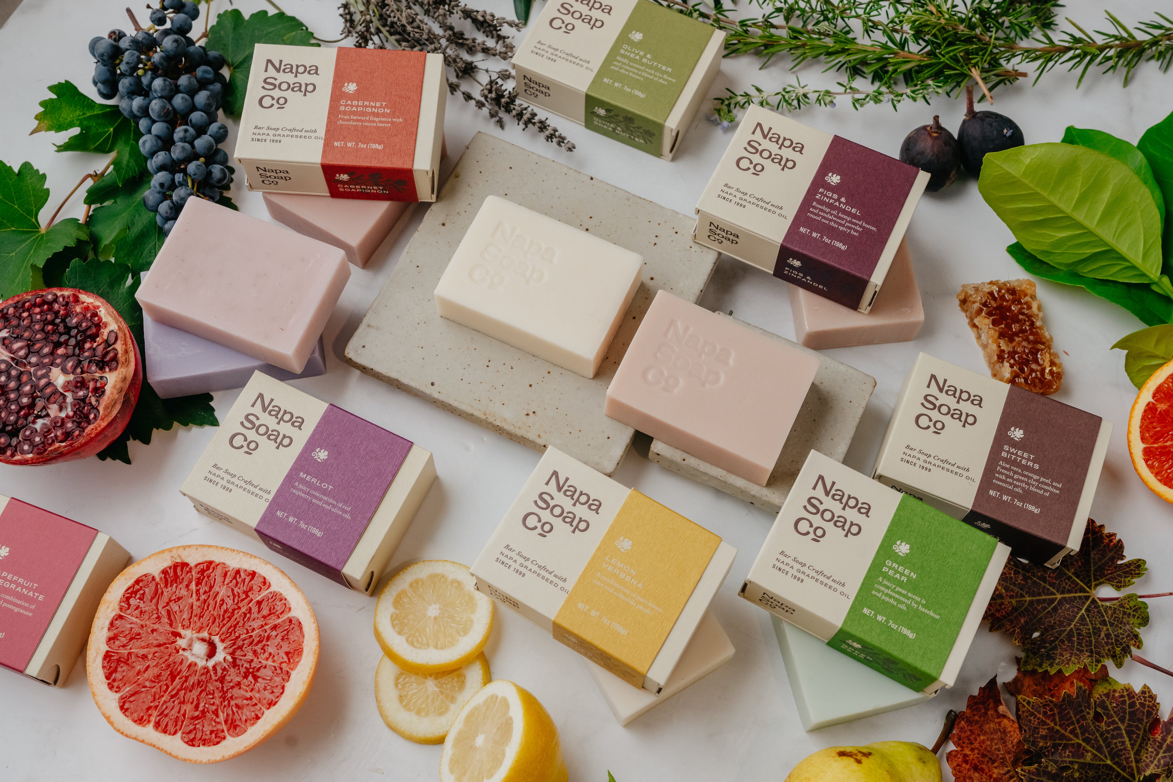 Napa Soap Co. soaps and packaging on a white surface with fruits and leaves.