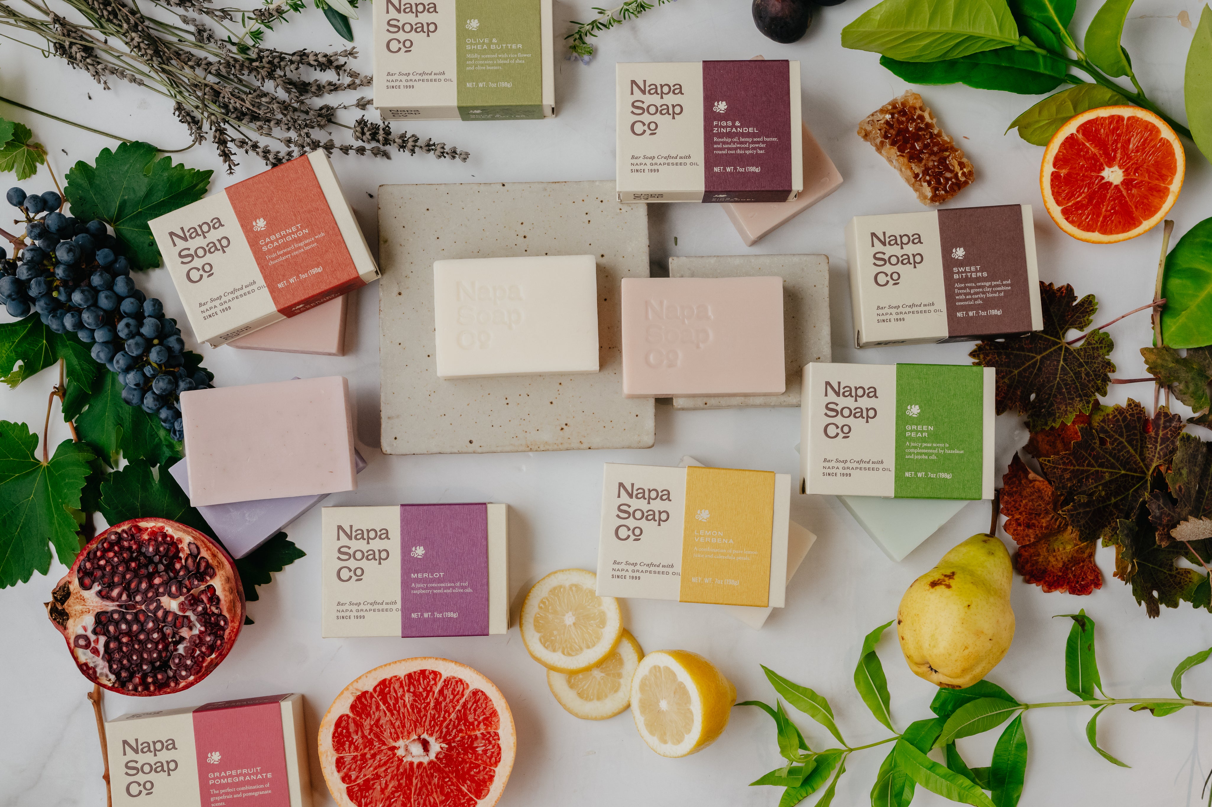 Napa Soap Co. soap bars and packaging on a white surface with fruits and leaves.