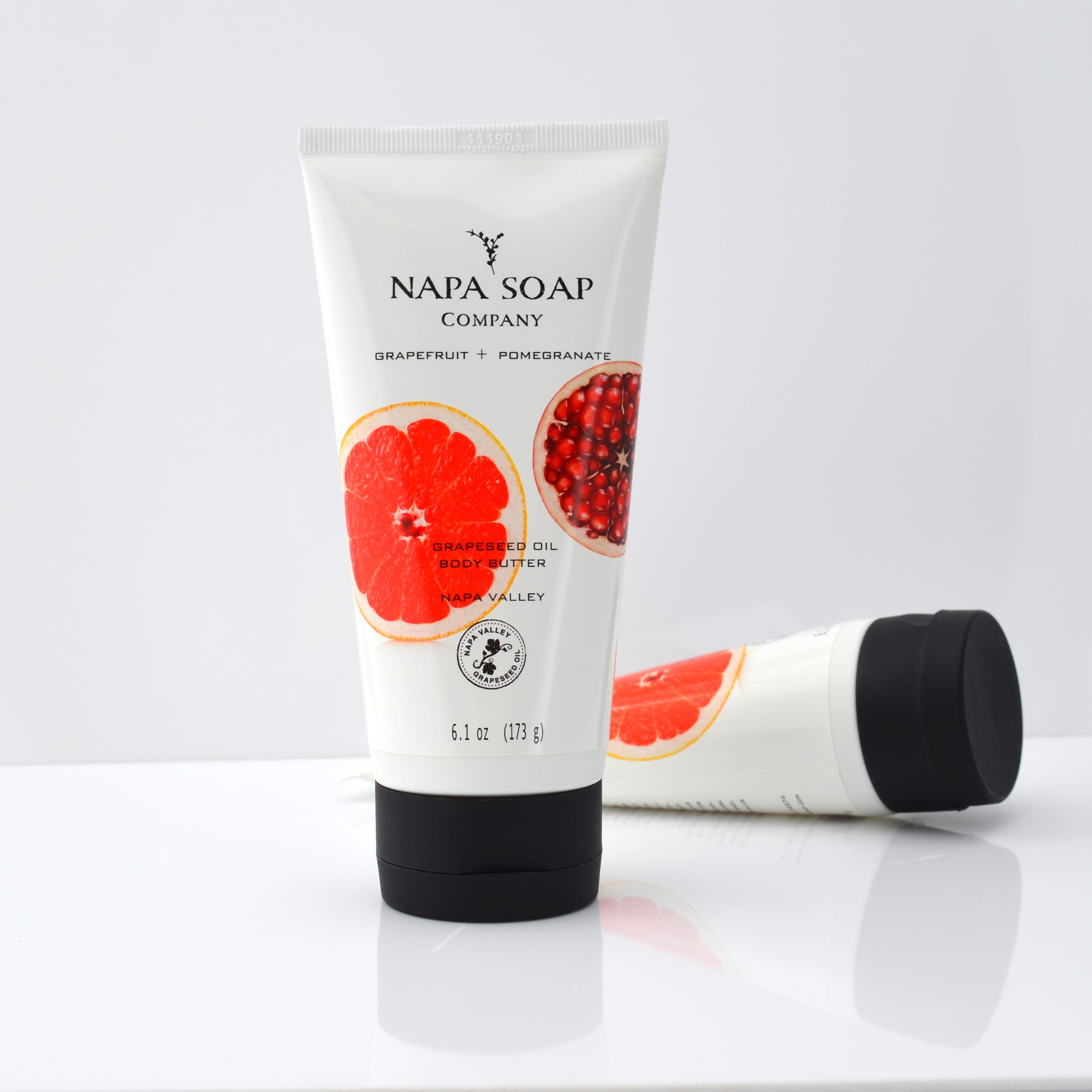 A tube of NAPA SOAP COMPANY body butter with grapefruit and pomegranate illustrations on the label, standing next to its cap.